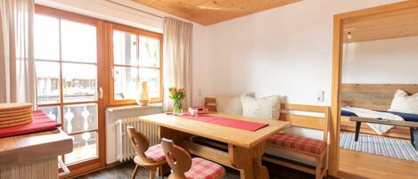 A cozy room with a wooden dining table, two chairs, a bench, and a bed with a wooden headboard.