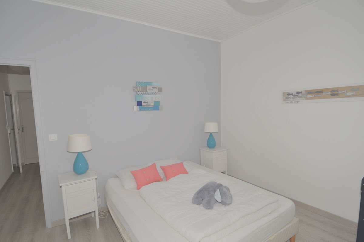Ein Schlafzimmer mit einem Bett, zwei Nachttischen, jeweils einer Lampe darauf, einer Wanddekoration und einer Tür links.