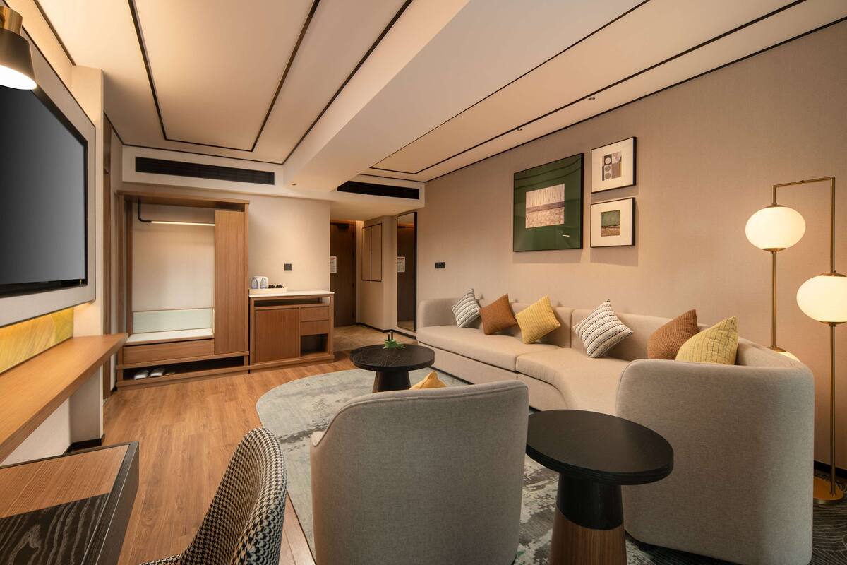A modern hotel room with a sofa, armchairs, a small table, and a TV.