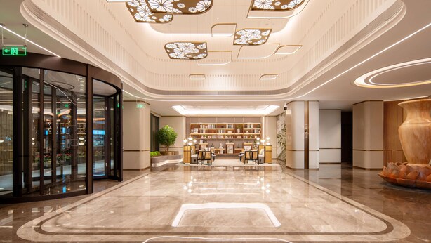 A modern lobby with a central seating area, a glass entrance, and a decorative ceiling.