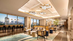 A modern hotel lobby with a city view, seating areas, and a bar.