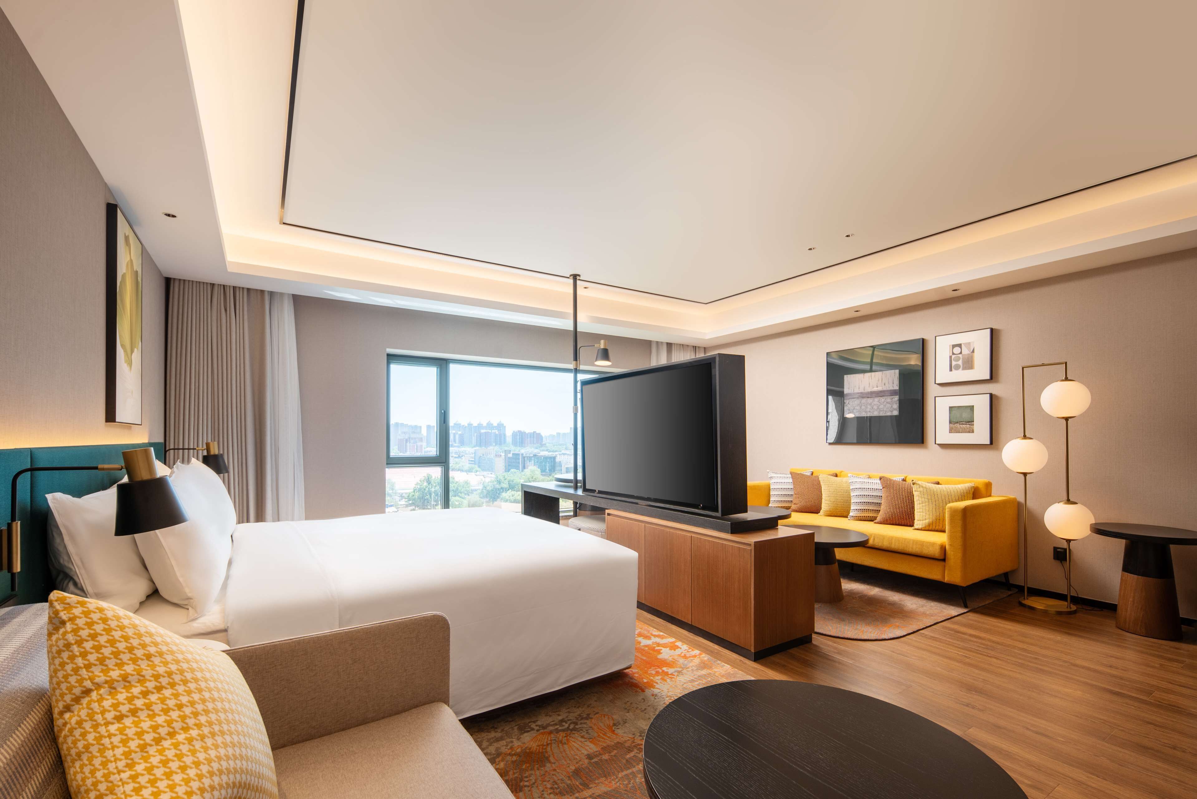 Ein modernes Hotelzimmer mit einem großen Bett, einer Couch, einem Fernseher und Blick auf die Stadt.