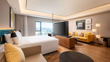 Ein modernes Hotelzimmer mit einem großen Bett, einer Couch, einem Fernseher und Blick auf die Stadt.