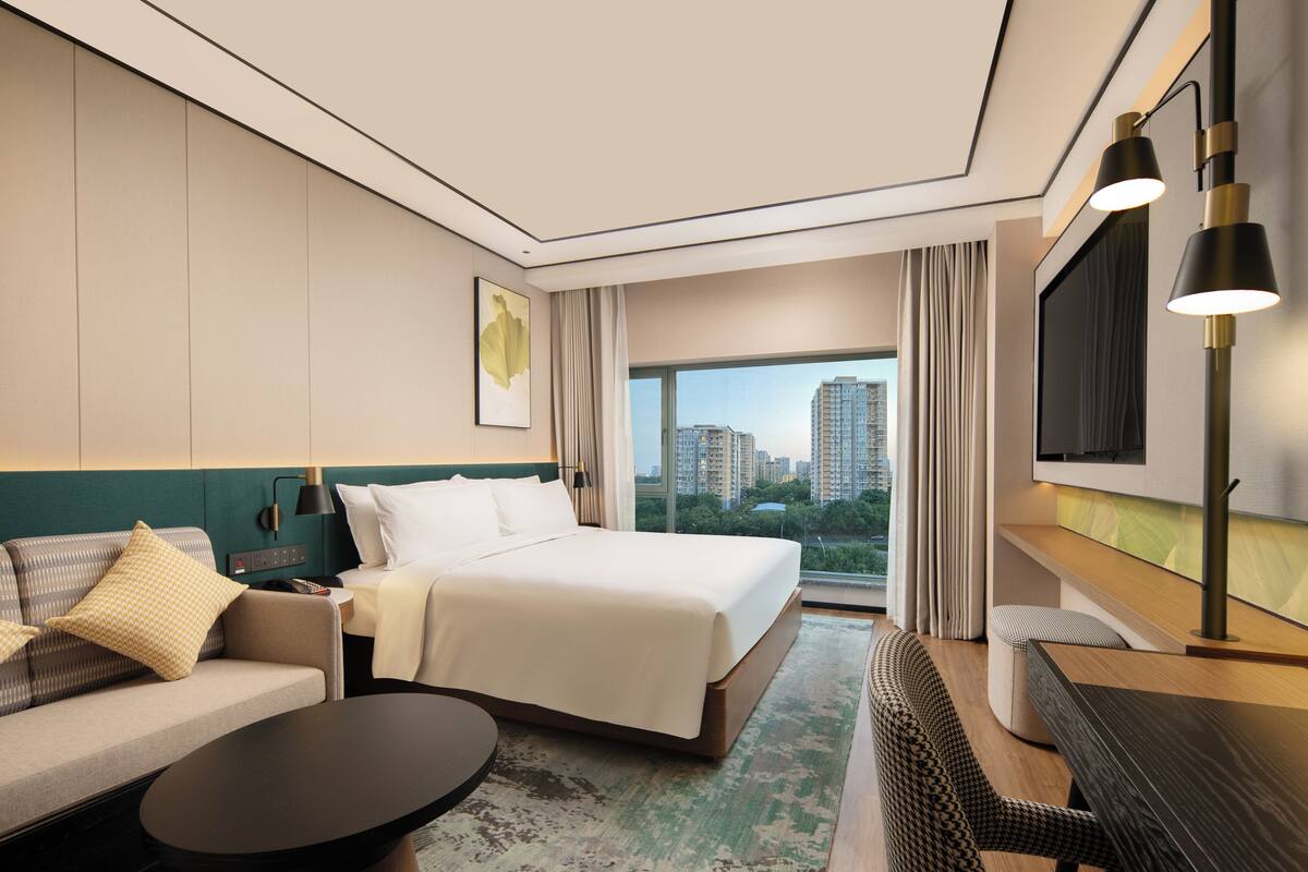A hotel room with a bed, sofa, coffee table, and a TV.