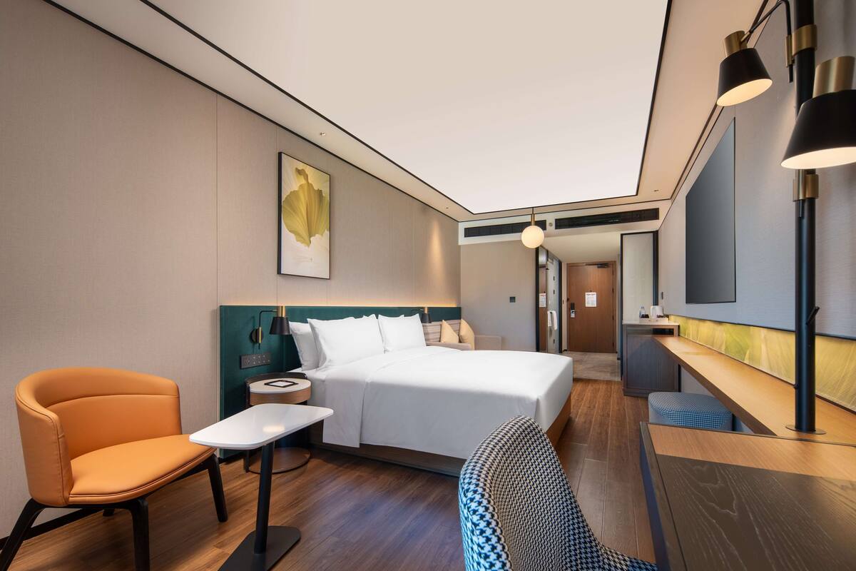 A modern hotel room with a bed, a desk, a chair, and a small table.