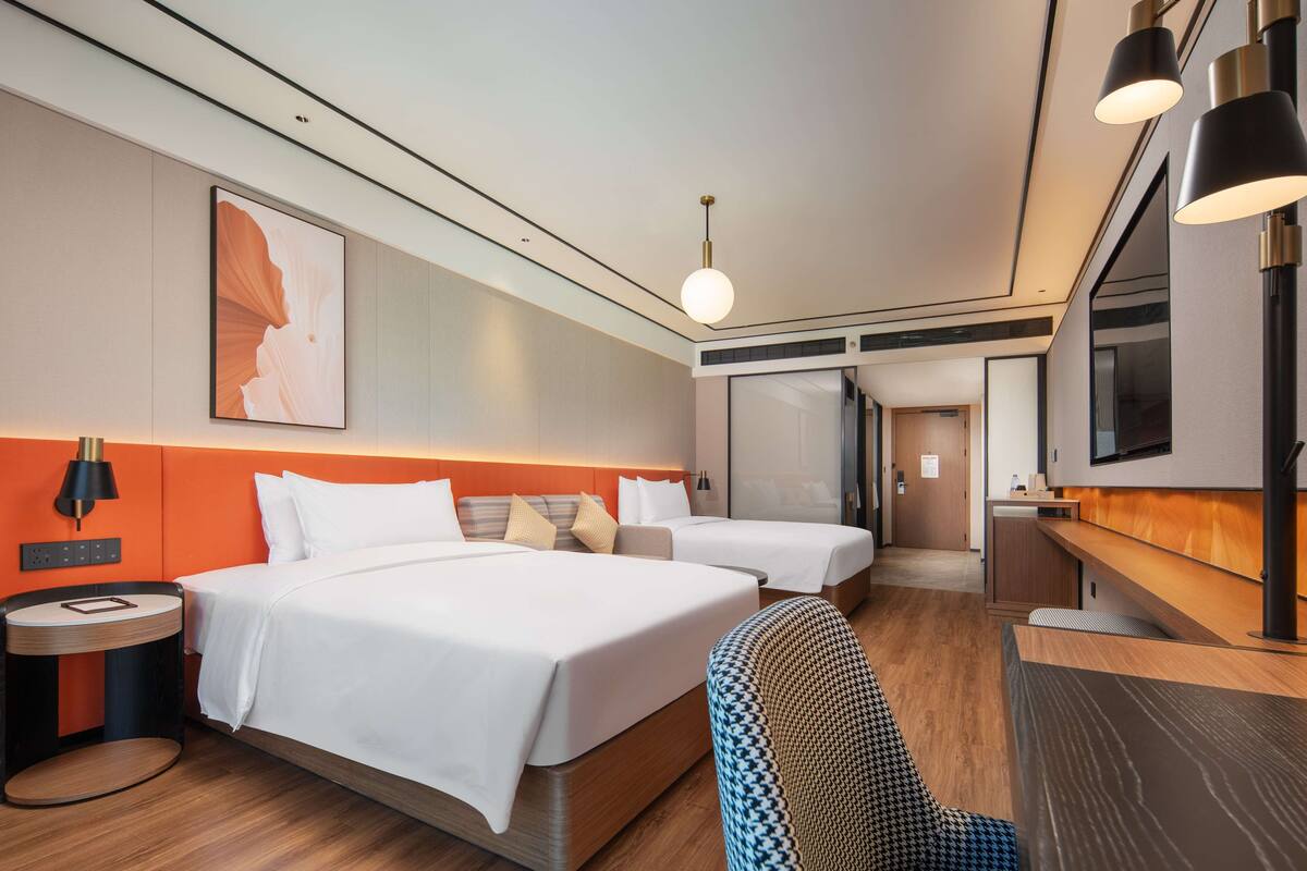 A hotel room with two beds, a desk, a chair, a TV, and a large artwork on the wall.