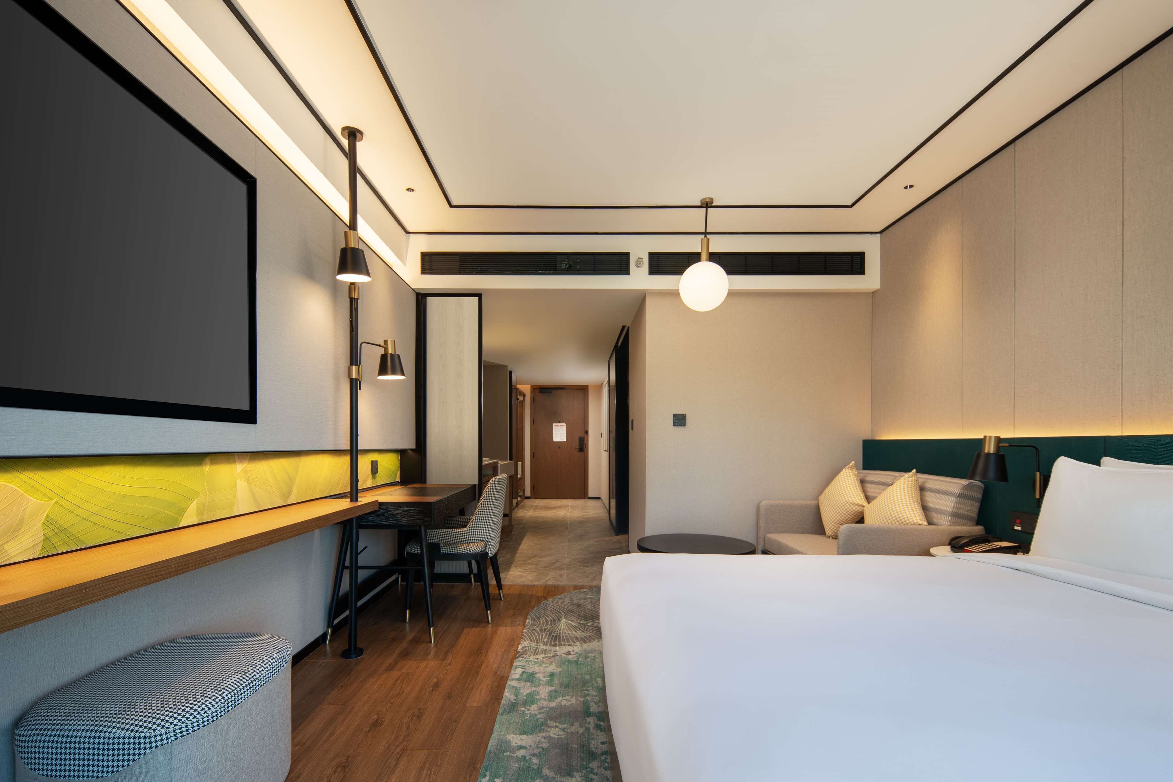 Una habitación de hotel moderna con una cama grande, un escritorio con una silla, un sofá y una pequeña zona de estar.