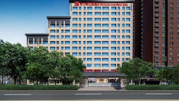 Experience the Hilton Garden Inn's sleek, modern design, featuring a covered entrance with a glass canopy and beautifully manicured hedges.