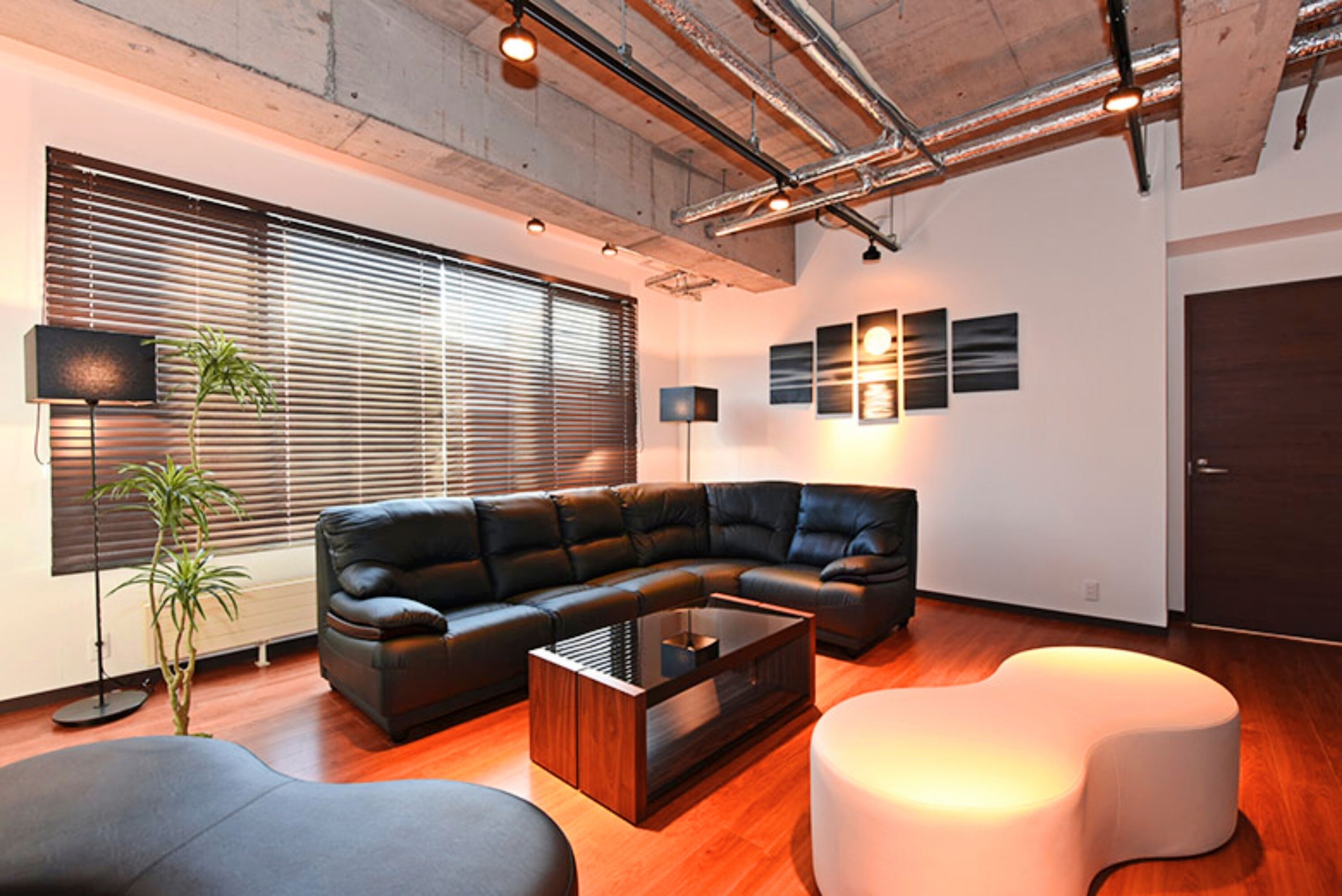 A modern living room with a sectional sofa, a glass coffee table, and a white ottoman.