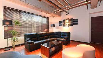 A modern living room with a sectional sofa, a glass coffee table, and a white ottoman.