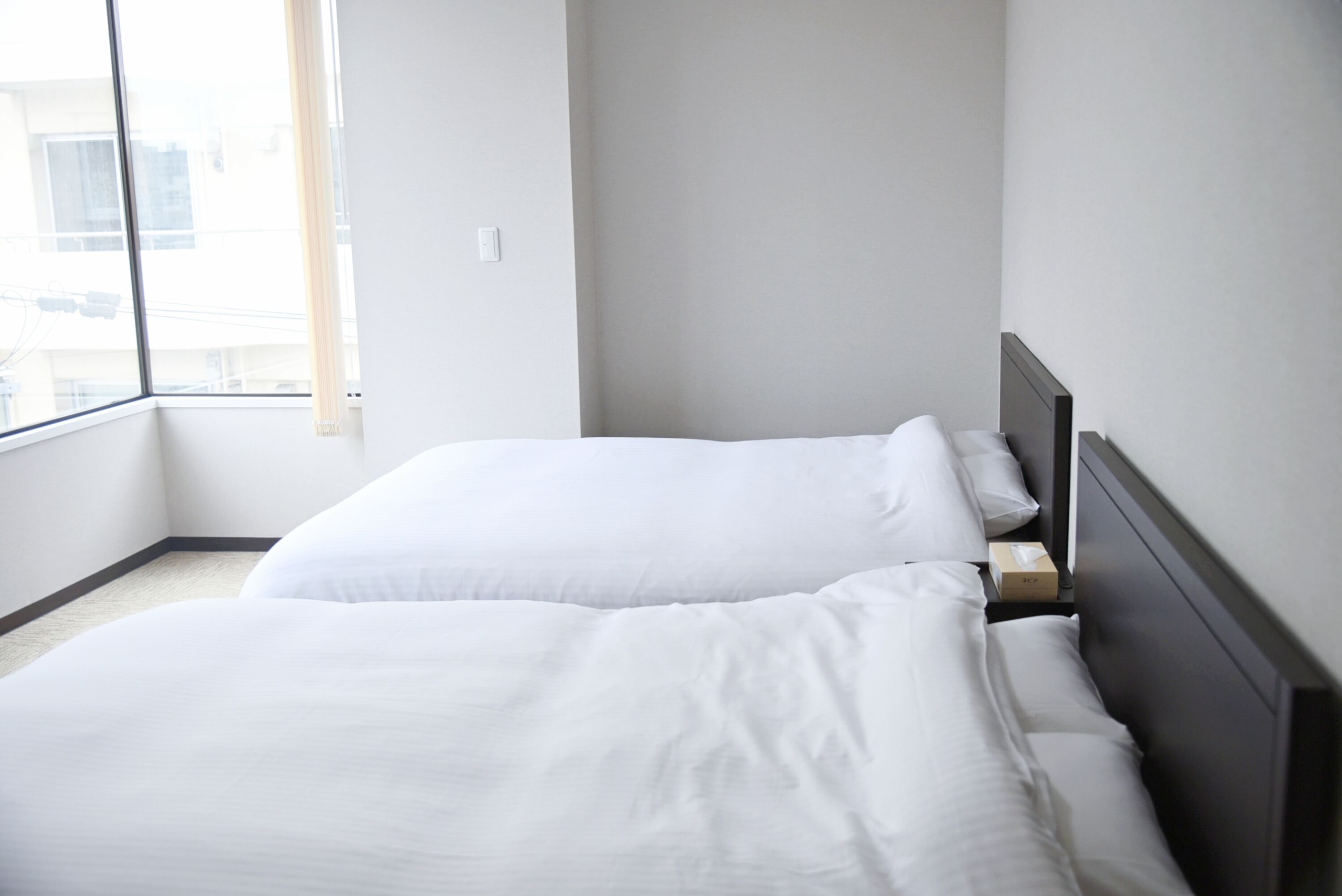 A hotel room with two beds, a window, and a view of buildings outside.