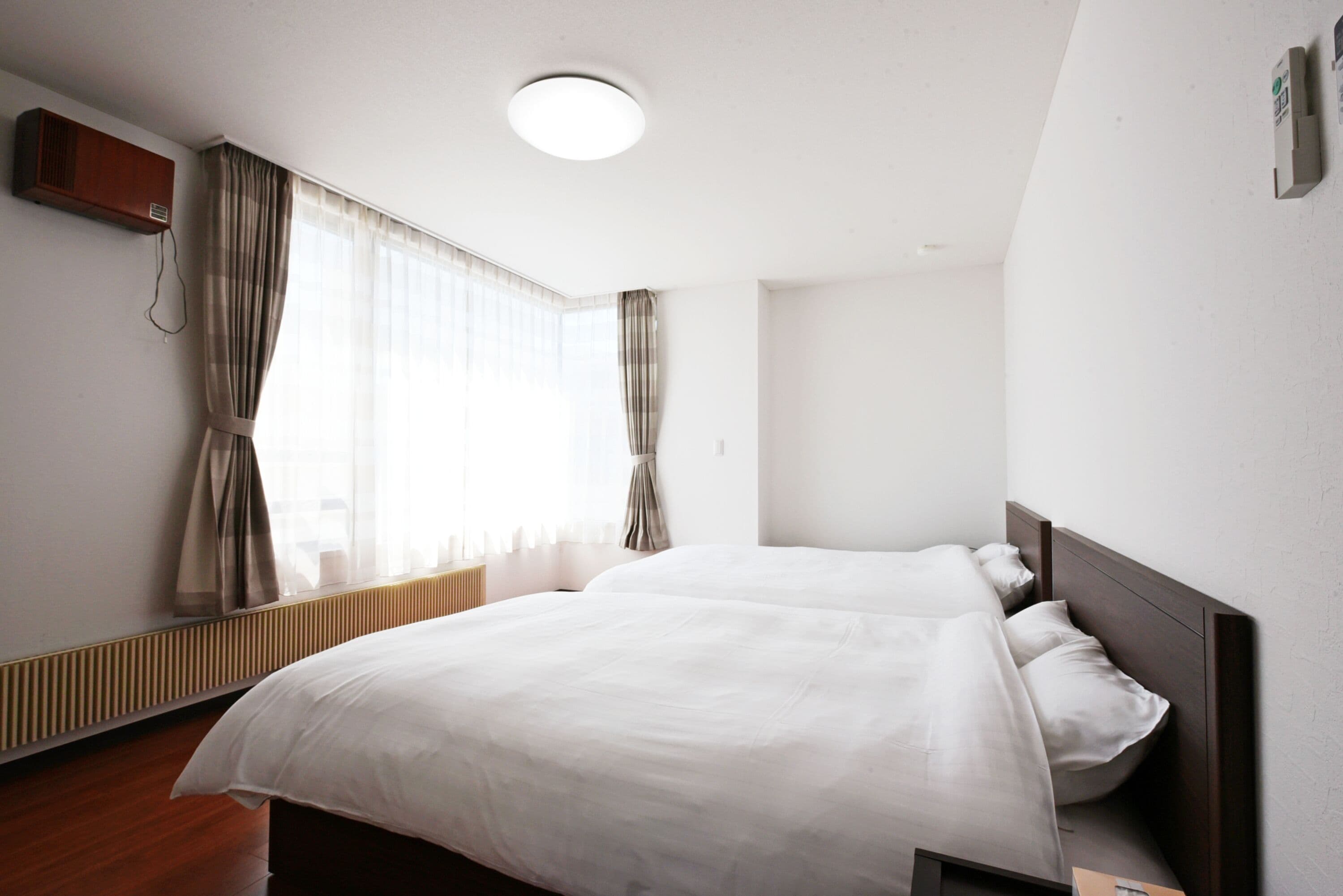A hotel room with a large bed, a radiator, a window with curtains, and a ceiling light.