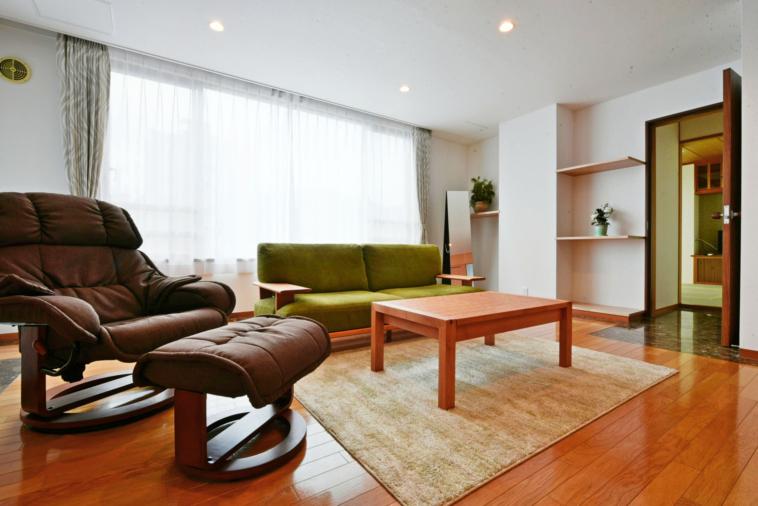 A modern living room with a brown leather recliner, a green sofa, and a wooden coffee table.