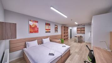 Een moderne hotelkamer met een groot bed, een bureau en een stoel. Er zijn planken en een prullenbak in de kamer.