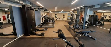 Un gimnasio con diverso equipo de ejercicio, incluyendo cintas de correr, máquinas de pesas y pesas libres.
