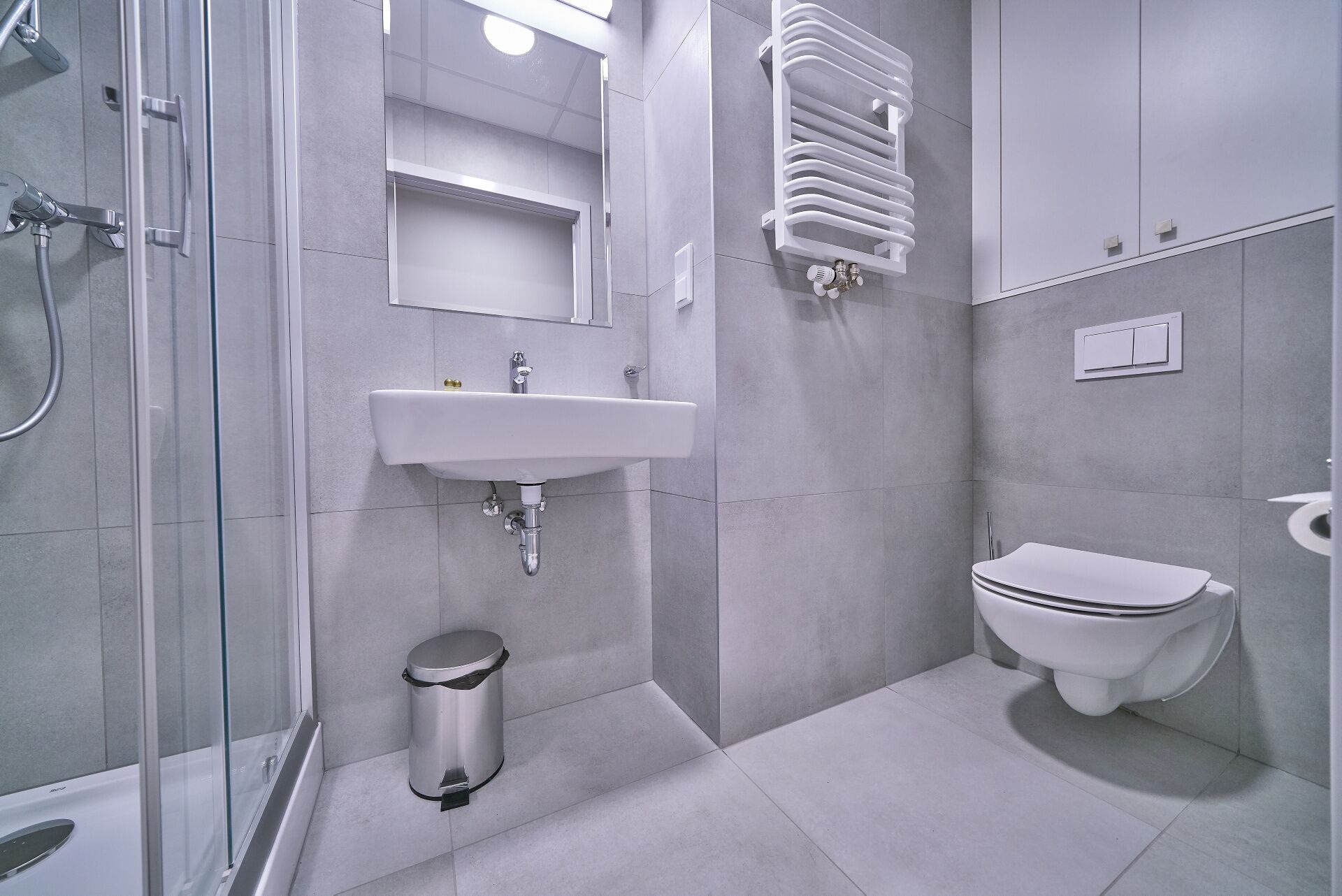 A modern bathroom with a glass shower enclosure, a white sink, a toilet, and a trash bin.