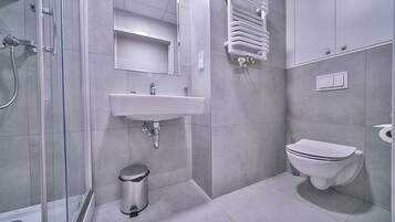 Un baño moderno con cabina de ducha de vidrio, un lavabo blanco, un inodoro y un cubo de basura.
