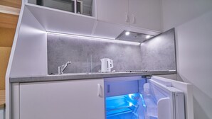 A compact kitchen with a built-in refrigerator, a kettle, and a microwave.