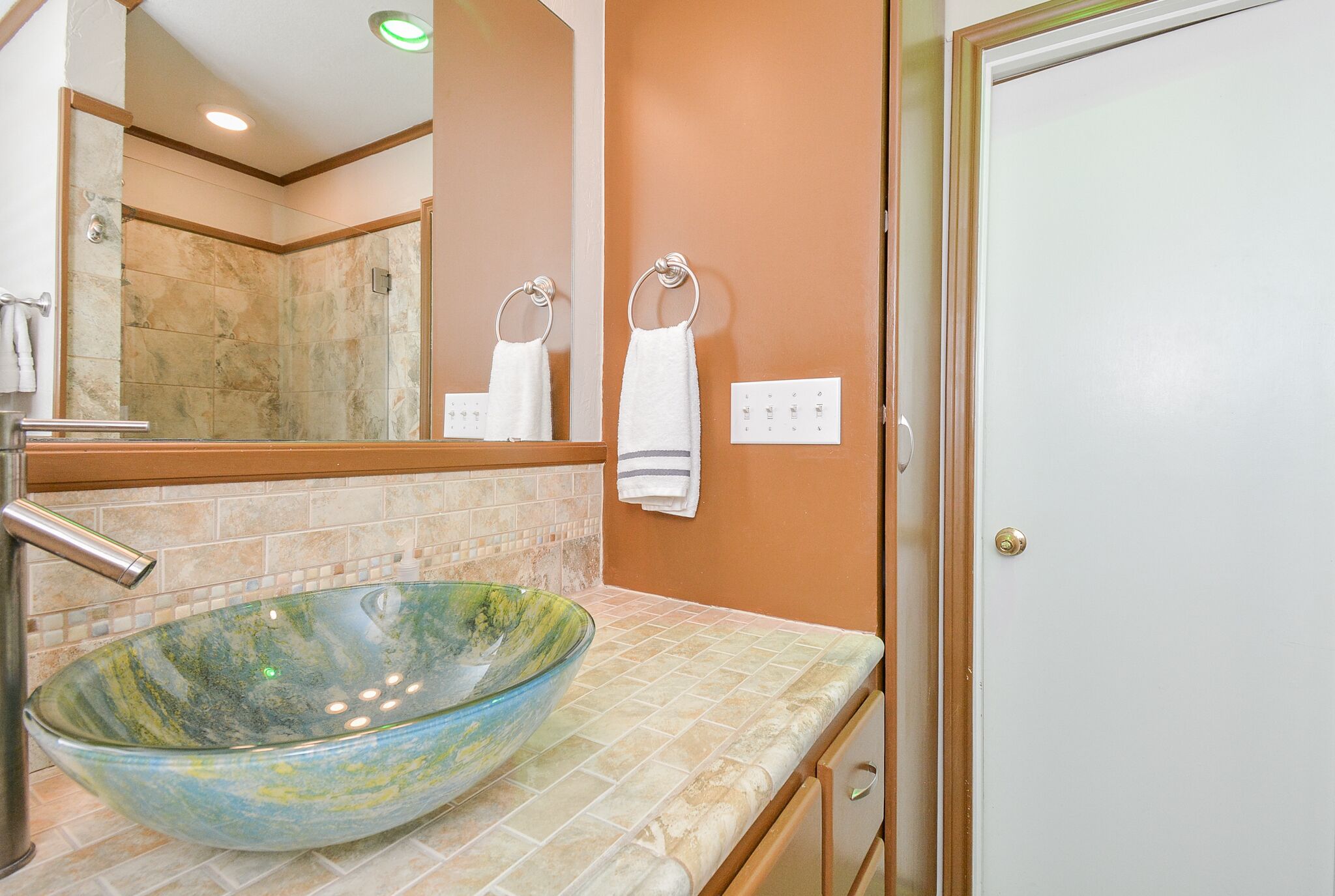Un bagno con un lavabo in vetro, uno specchio e un porta asciugamani.