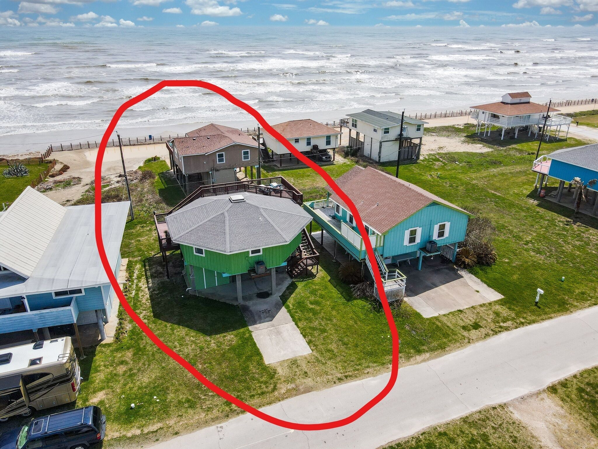Vue aérienne d’une zone résidentielle côtière, avec des maisons, une plage et une vaste étendue d’eau.