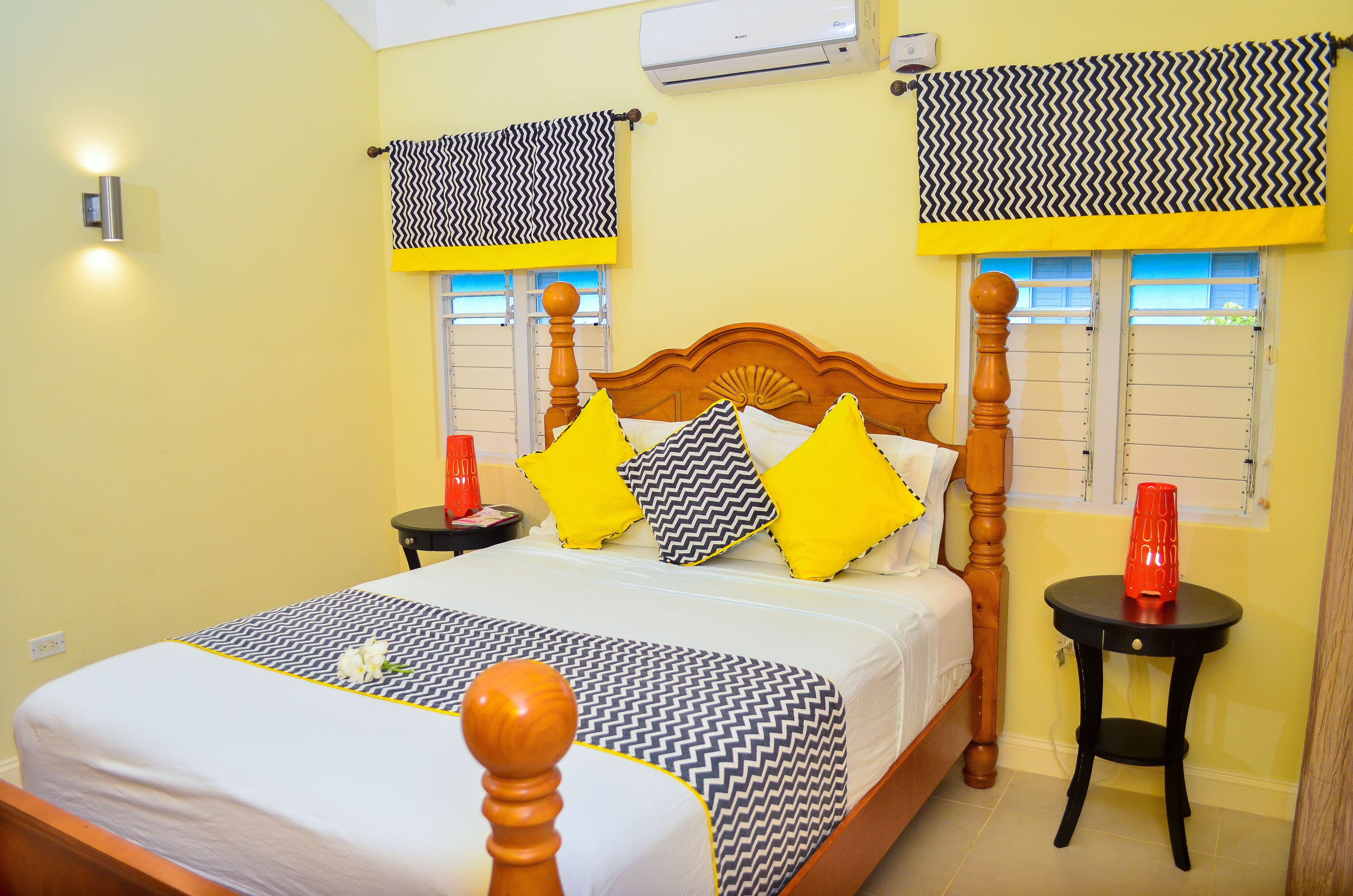 A neatly made bed with patterned bedding, a wooden headboard, and two bedside tables with red vases.