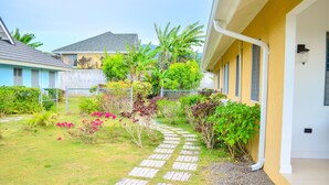 Un chemin de jardin qui mène à un bâtiment à la façade jaune et doté de nombreuses fenêtres.