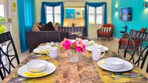 Un coin repas avec une table dressée pour quatre personnes, un vase rempli de fleurs et un téléviseur fixé au mur.