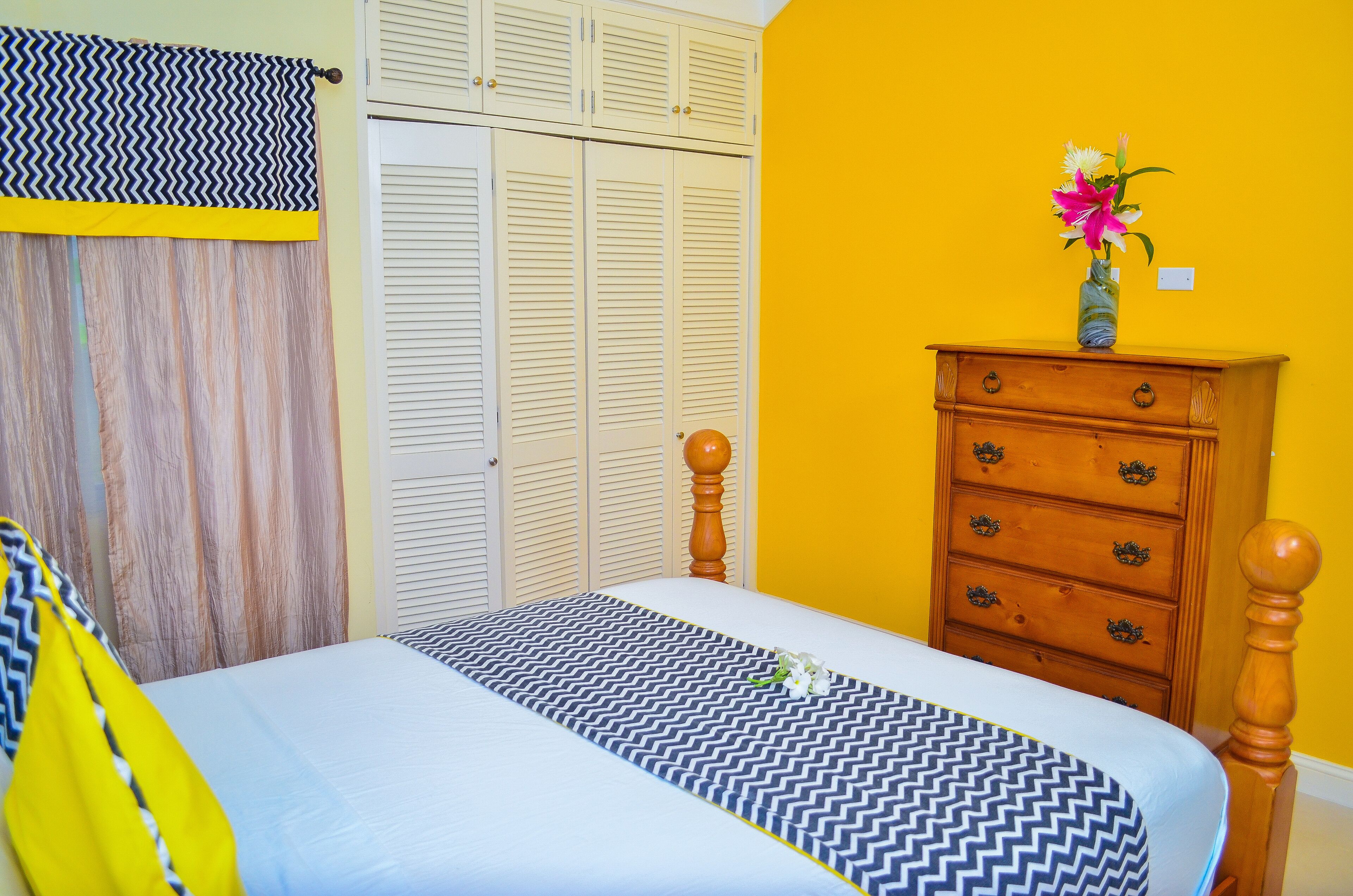 A bedroom with a bed, a wooden dresser, a closet, and a yellow wall.