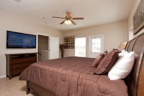 Quarto com cama, ventoinha no teto, televisão na parede e porta para outro cômodo.
