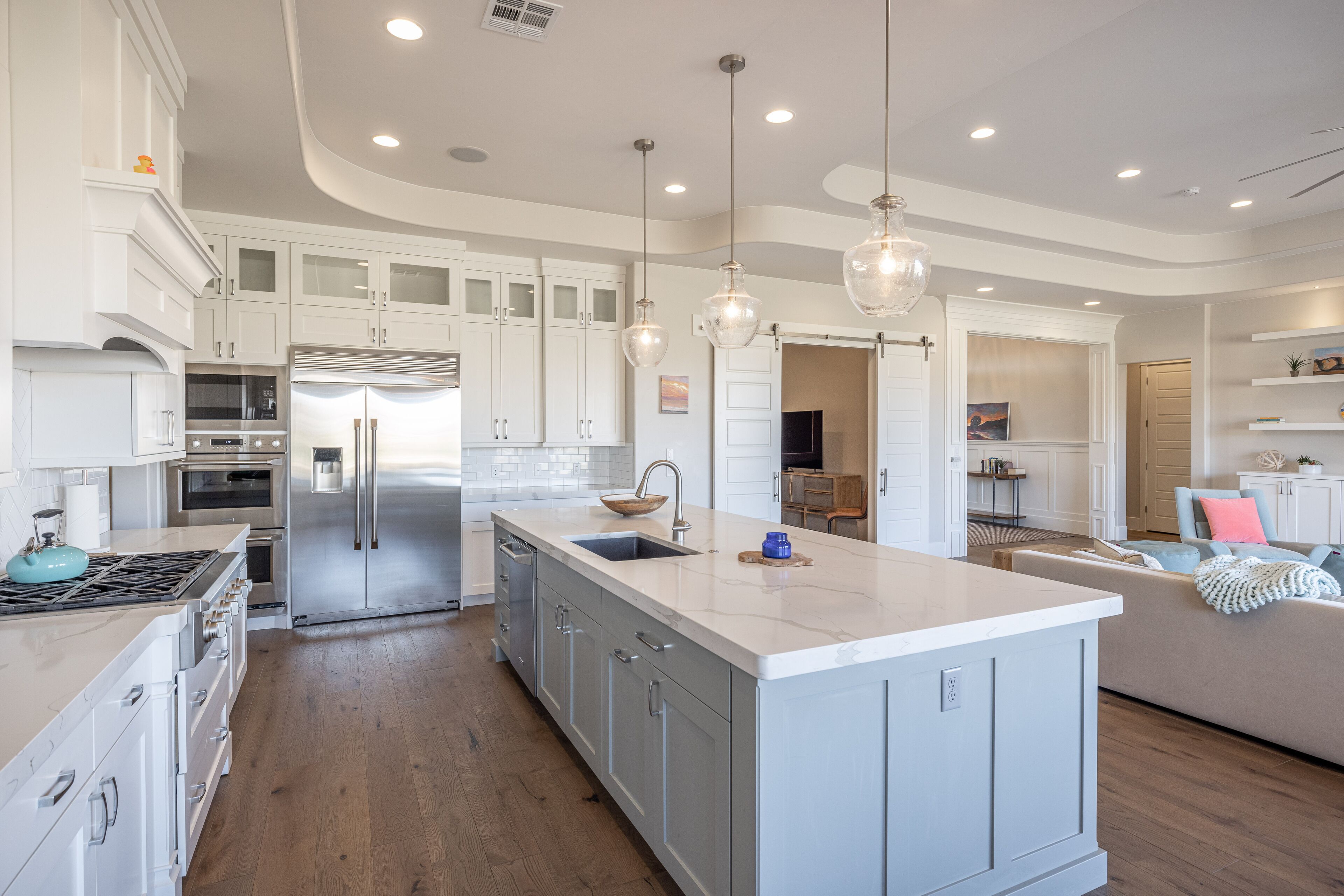 Une cuisine spacieuse avec des meubles blancs, un îlot central, des appareils en acier inoxydable et des luminaires suspendus.