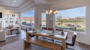 Un salon spacieux avec une grande table à manger en bois, des sièges confortables et une vue sur un terrain de golf et les montagnes.