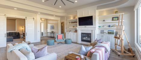 A spacious living room with a fireplace, a television, and a painting on easels.