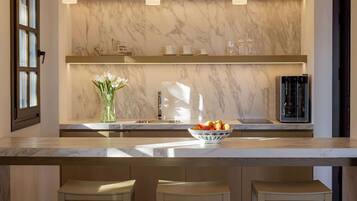 A modern kitchen with marble countertops, a central island with a bowl of fruit, and built-in shelves with decorative items.