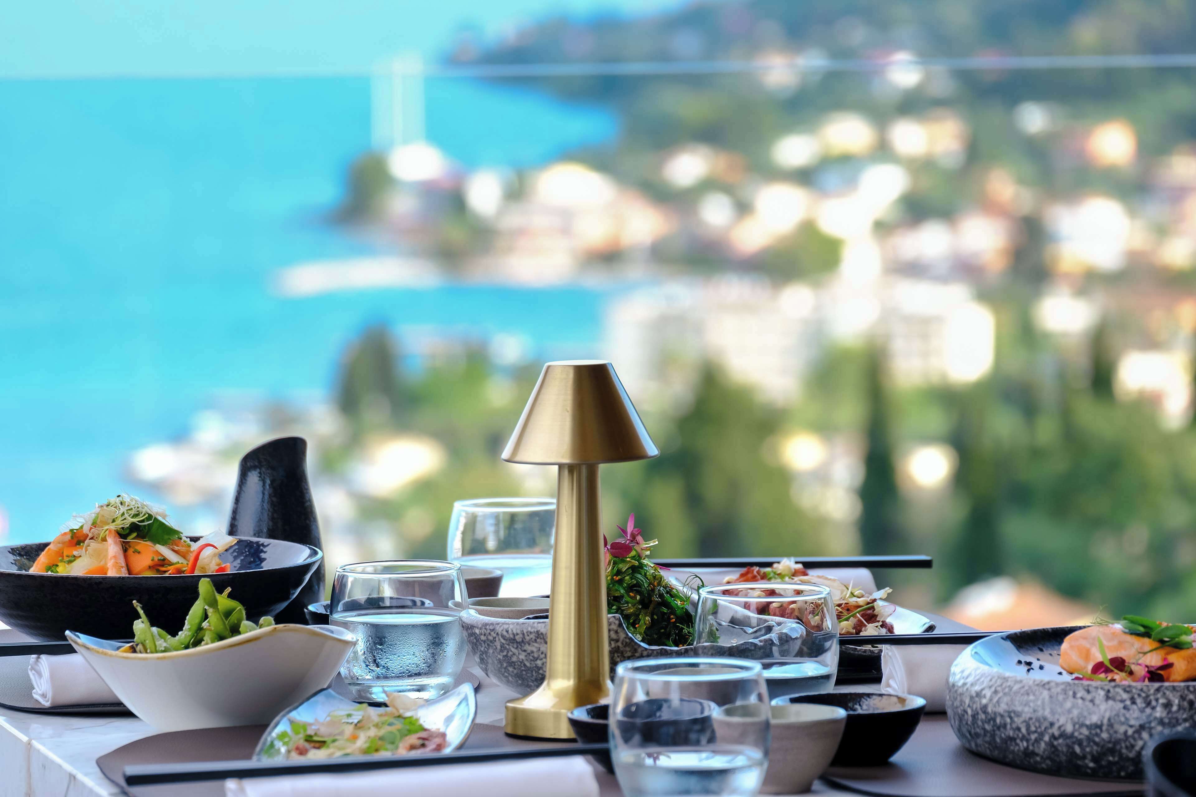 A table set with various dishes and glasses, overlooking a scenic coastal view.