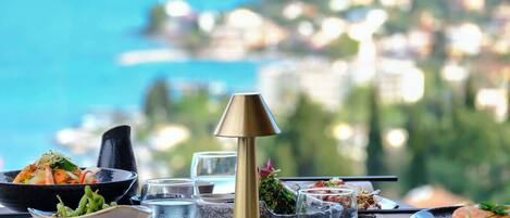 Una mesa servida con diversos platos y vasos, con vistas a un paisaje costero.