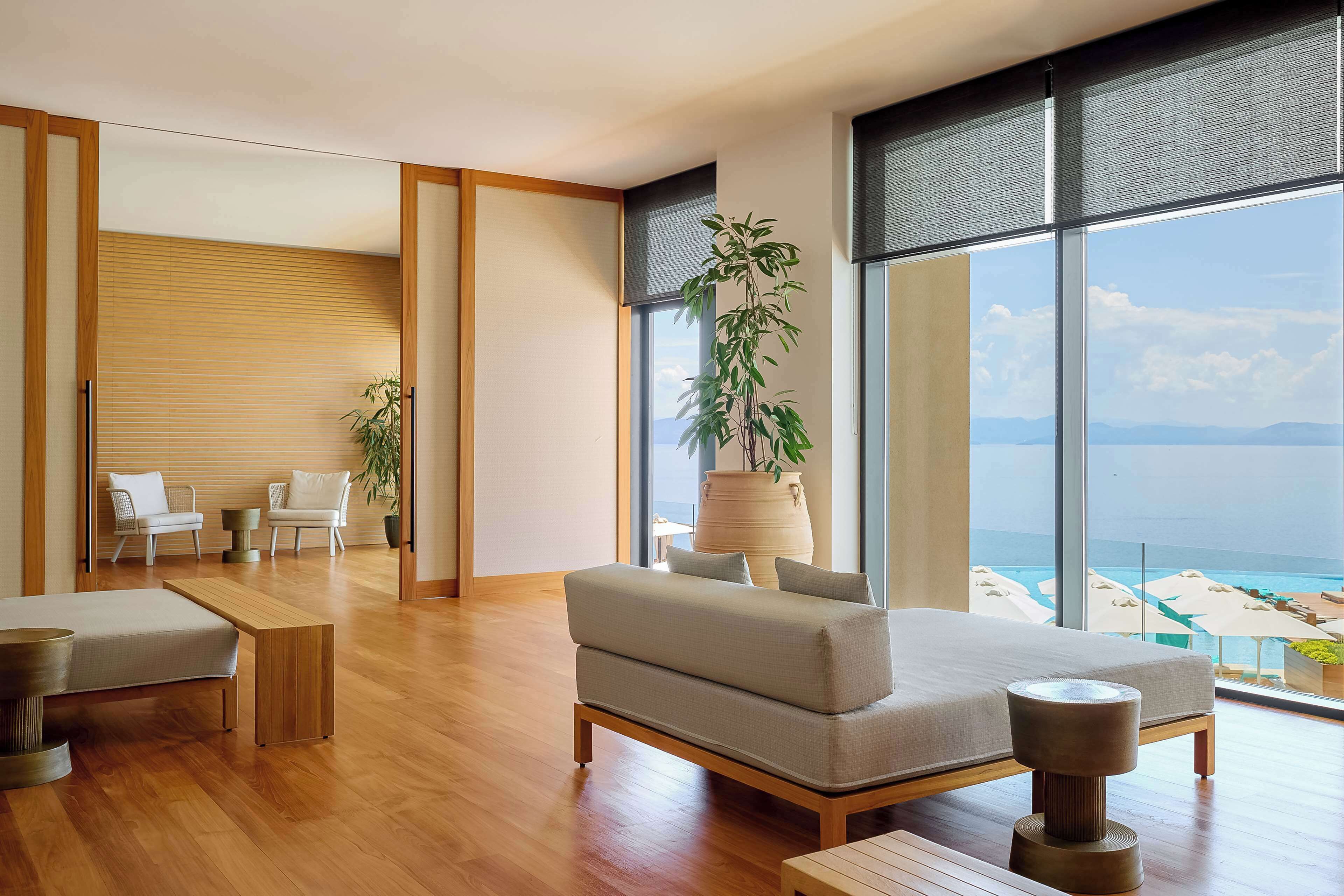 A modern living room with a large window, wooden flooring, a sofa, a coffee table, and a view of the ocean.