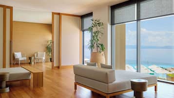 A modern living room with a large window, wooden flooring, a sofa, a coffee table, and a view of the ocean.