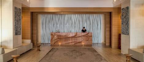 Una moderna zona de recepción con un mostrador de madera, un fondo estampado y una alfombra central.