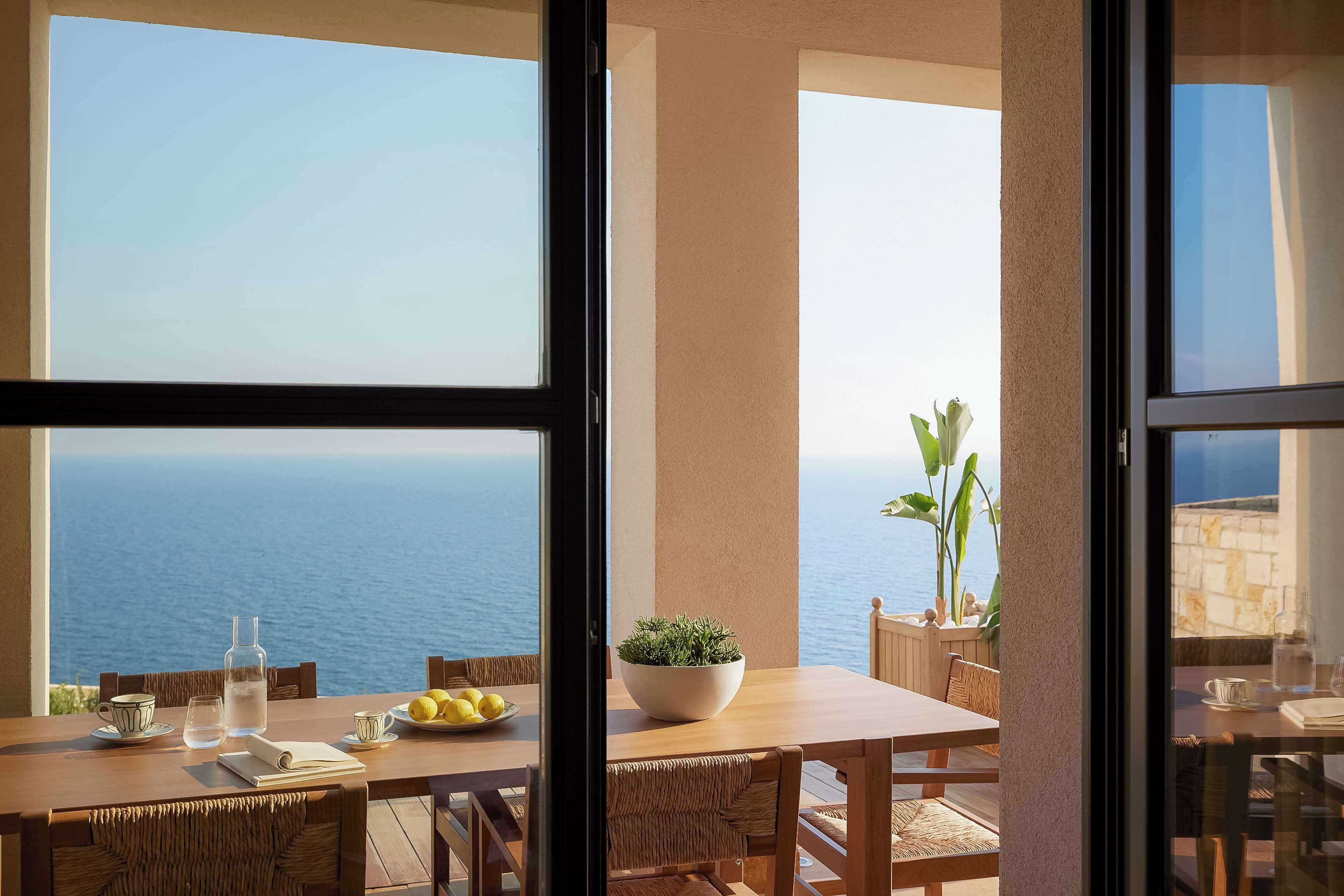 A dining area with a view of the sea, a table with a bowl of lemons, and a potted plant.