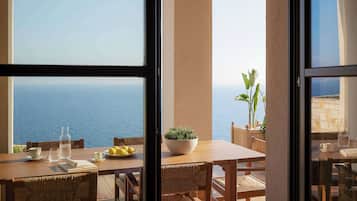 A dining area with a view of the sea, a table with a bowl of lemons, and a potted plant.