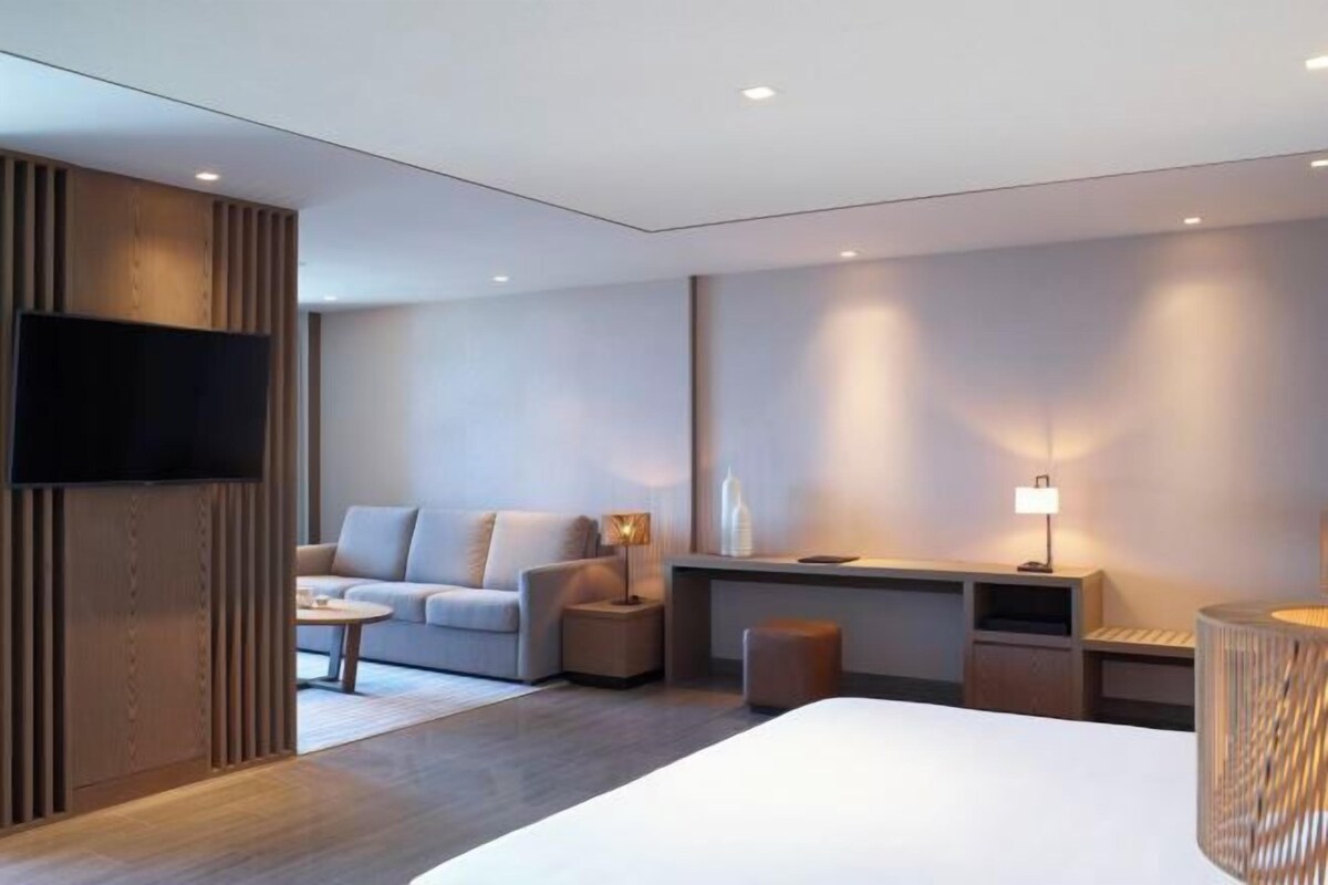 A modern hotel room with a large bed, a sofa, a desk, and a television.