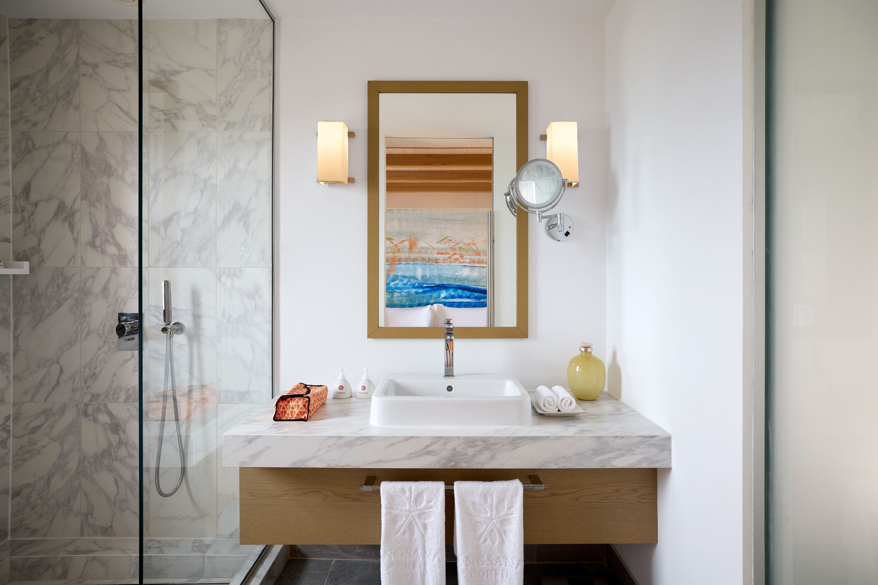A bathroom with a glass shower enclosure, a marble sink, and a wooden vanity.