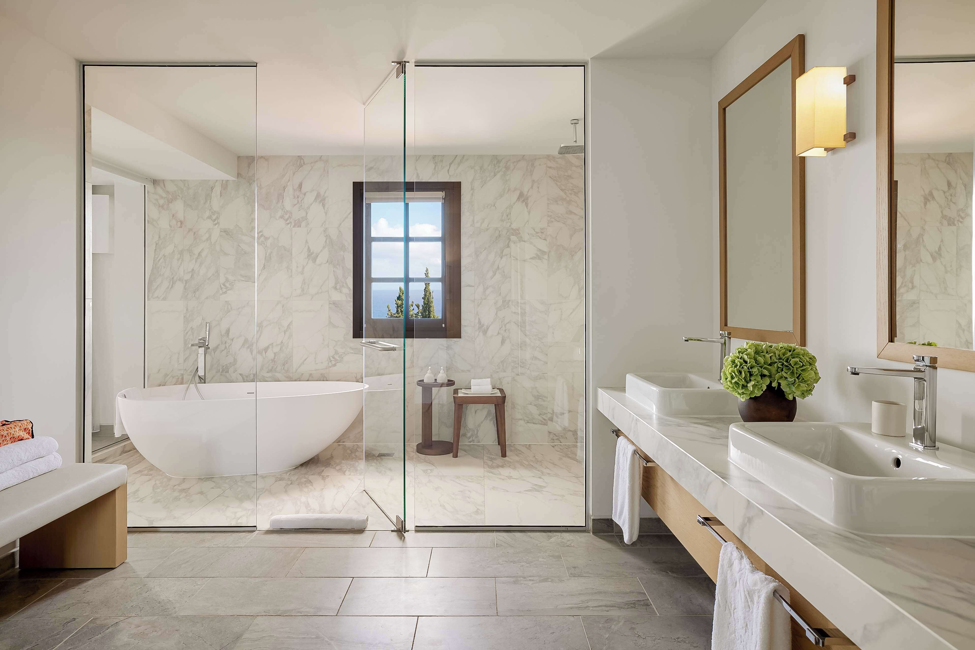 A modern bathroom with a freestanding bathtub, a large mirror, and a window with a view.