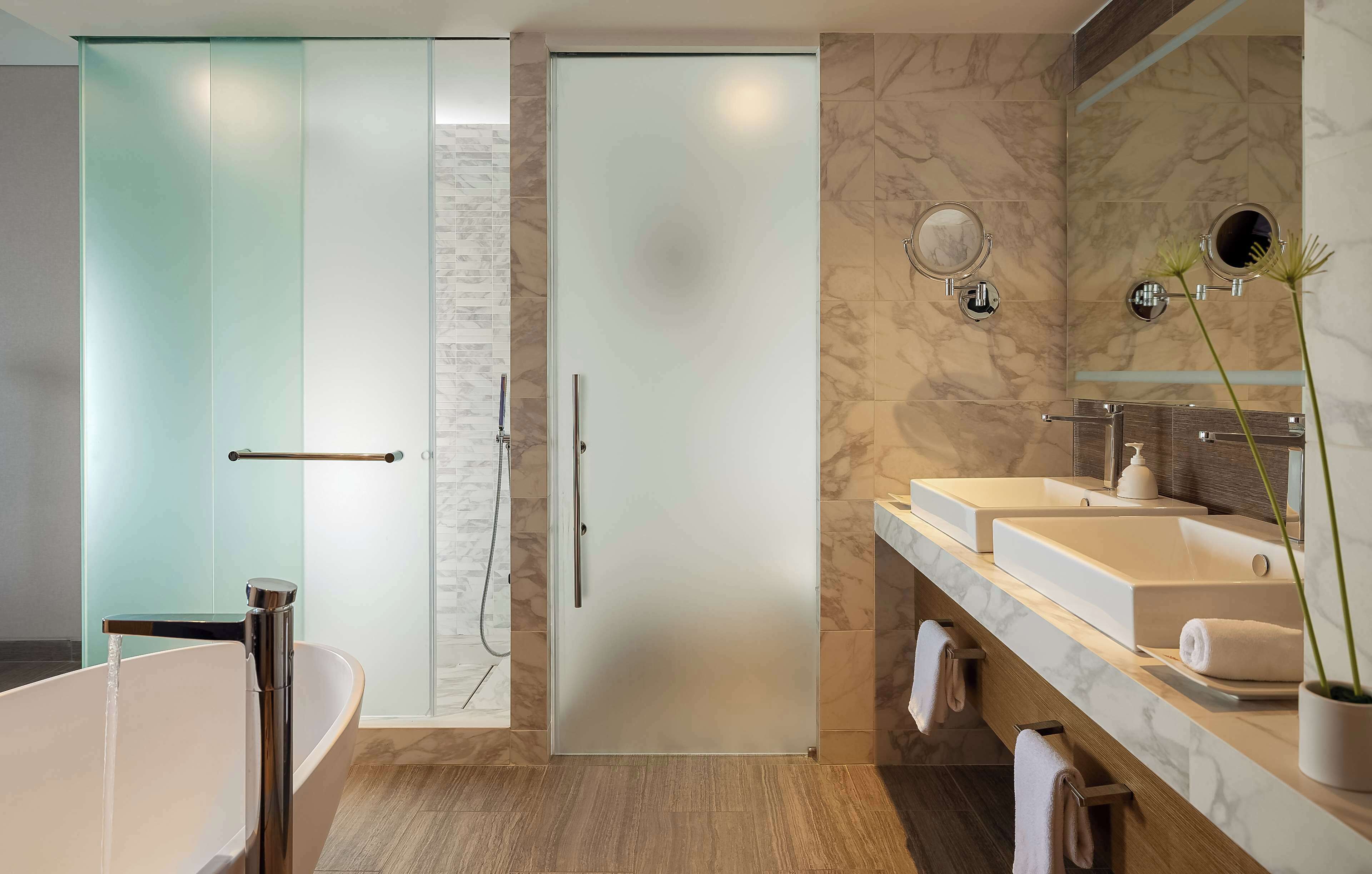 A modern bathroom with a glass shower enclosure, a freestanding bathtub, and a vanity with two sinks.