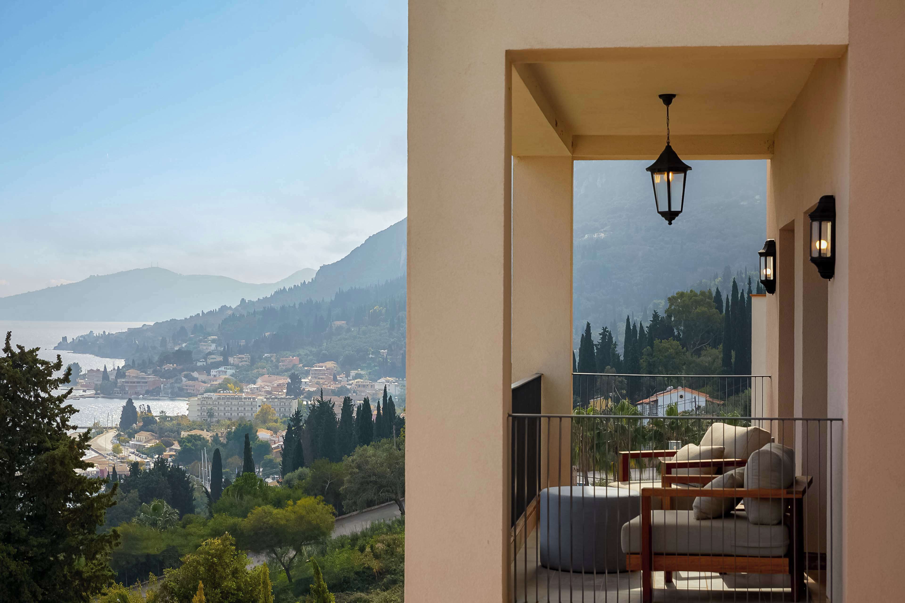 Un balcon donnant sur une ville côtière, un luminaire suspendu et deux fauteuils rembourrés.