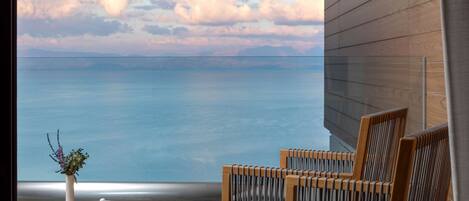 A balcony with a view of the sea, wooden chairs, a small table with a vase and a bowl.
