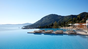 A infinity pool with lounge chairs, a mountain backdrop, and a clear view of the sea.