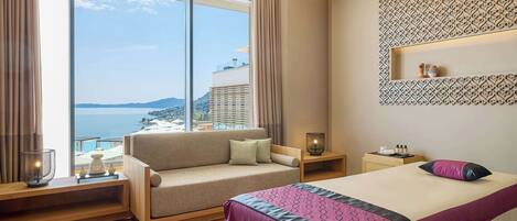 Una habitación de hotel moderna con un ventanal grande, un sofá, una cama y una mesita de noche.