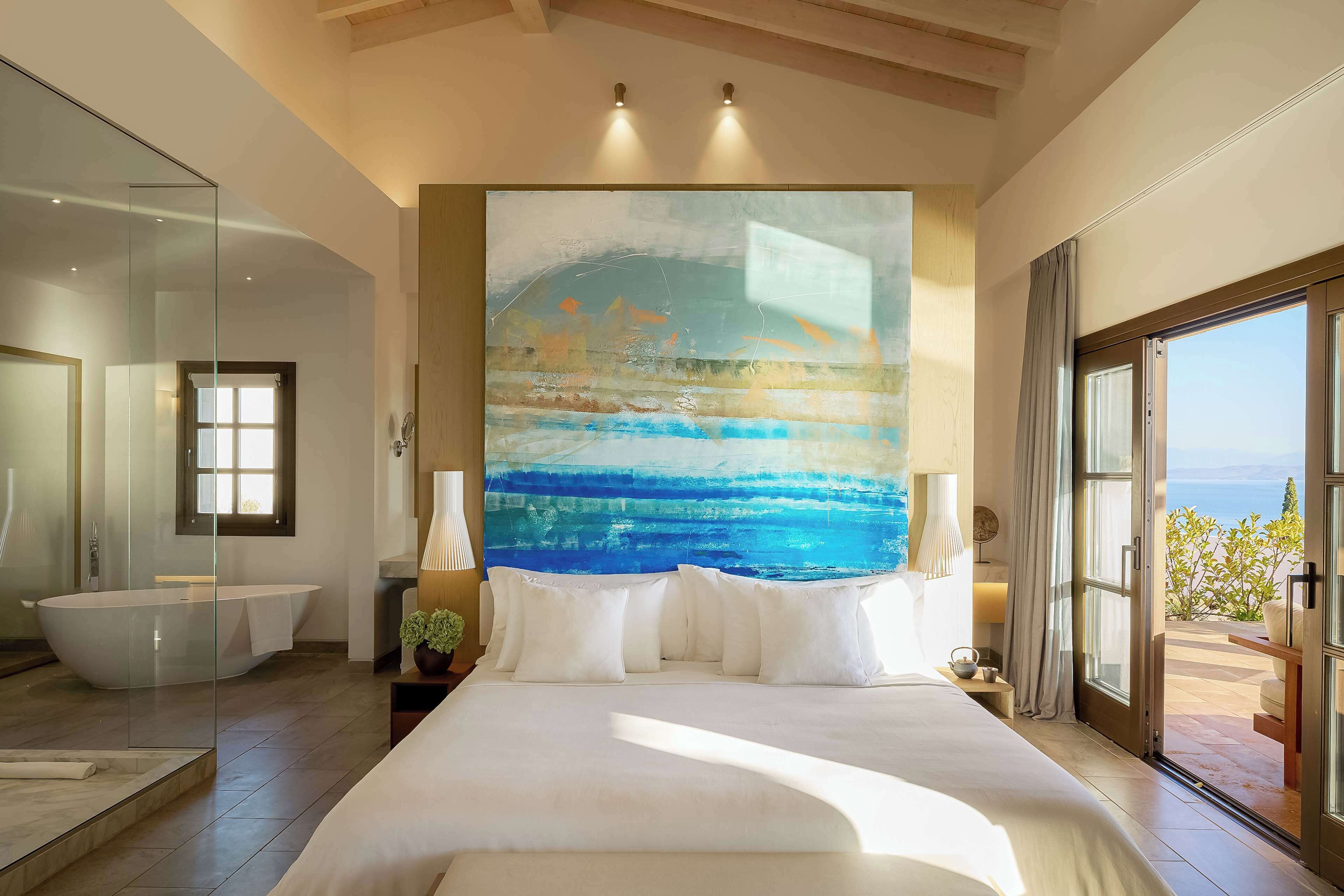 A modern hotel room with a large bed, a bathtub, and a view of the sea.