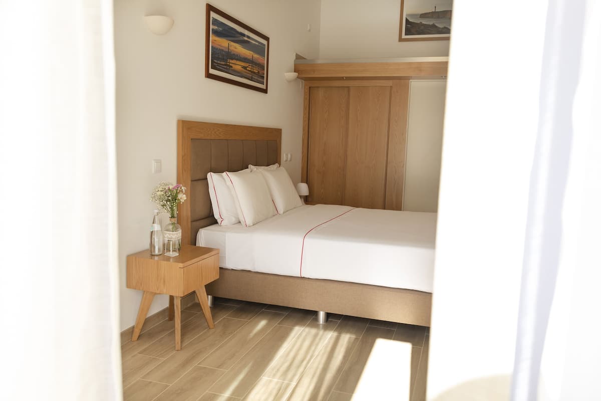 A bedroom with a bed, bedside table, lamp, and a painting on the wall.